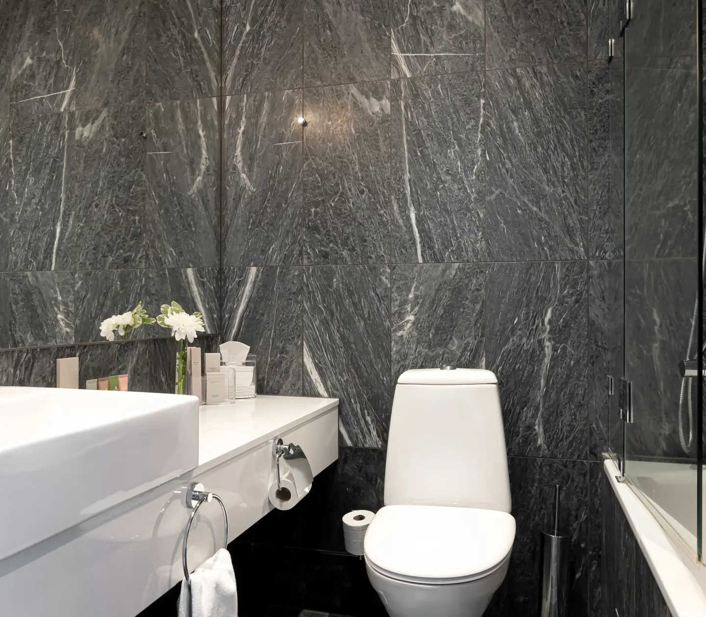 Bathroom with dark tiles with bathtub, toilet and sink